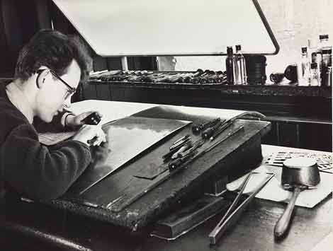 Photo of man engraving with tools on desk beside him