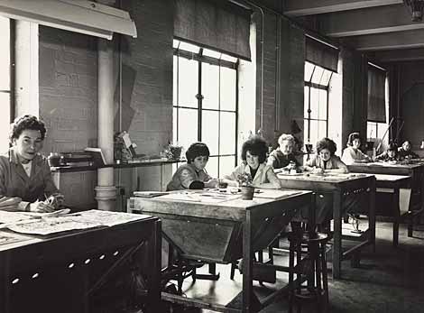 Photo of women seated at work tables looking up