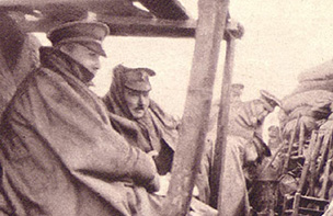 Soldiers huddled in rain capes in a trench