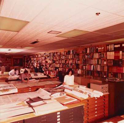 Colour photo of a large room with shelves of books and large tables with maps