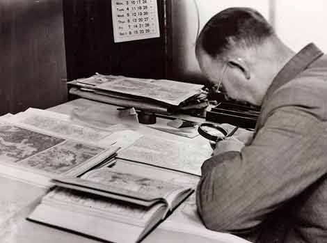 Photo of man working on a map and using magnifying glass