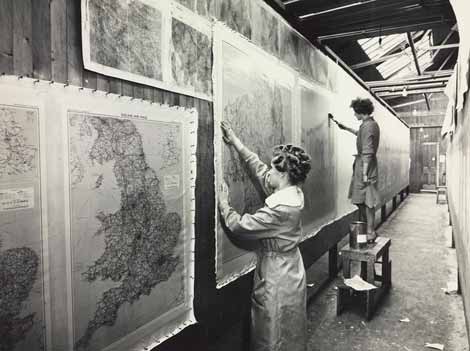 Photo of a women varnishing maps hung on a wall