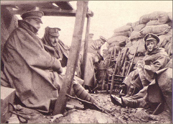 Soldiers huddled in rain capes in a trench
